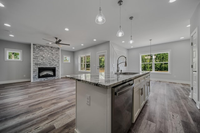 kitchen with a center island with sink, hanging light fixtures, dishwasher, light stone countertops, and sink