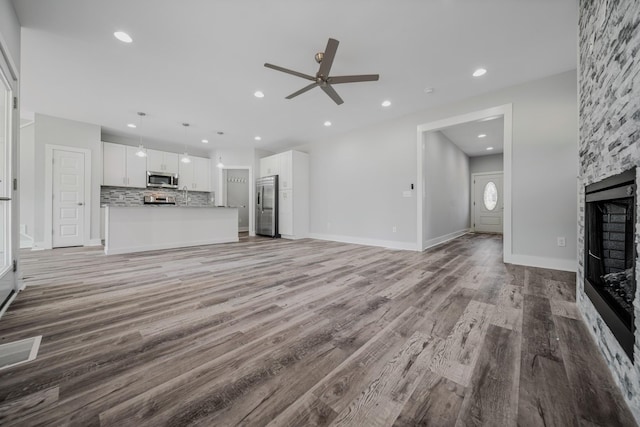 unfurnished living room with ceiling fan, light hardwood / wood-style flooring, and a stone fireplace