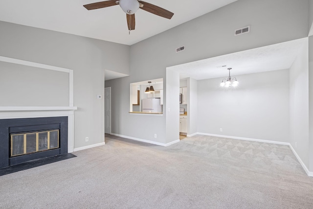 unfurnished living room with ceiling fan with notable chandelier, vaulted ceiling, and light colored carpet