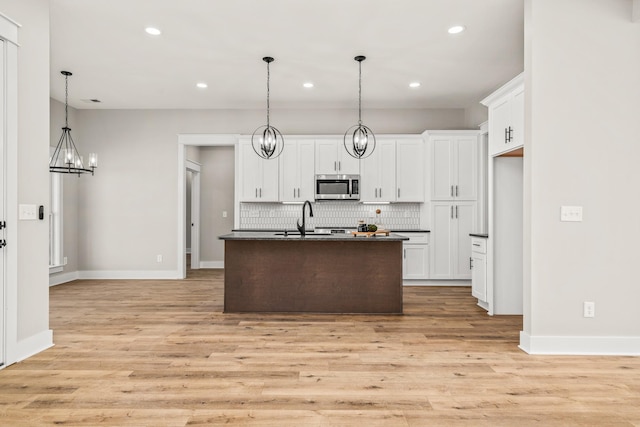 kitchen featuring backsplash, white cabinets, a kitchen island with sink, and a chandelier