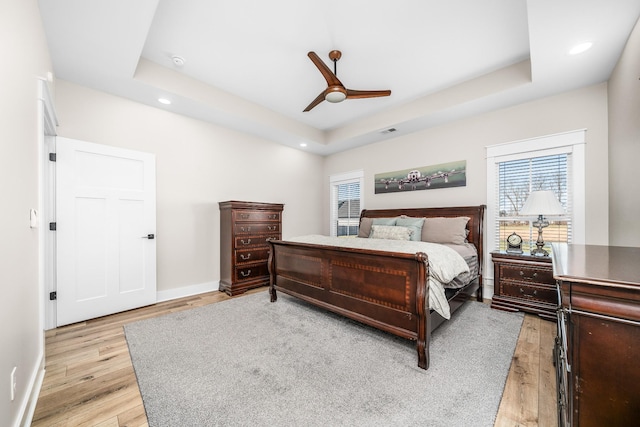 bedroom with light wood-type flooring, a tray ceiling, and ceiling fan