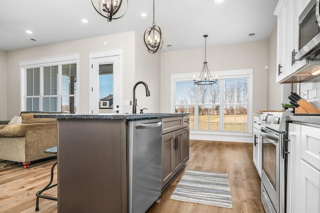 kitchen with stainless steel appliances, white cabinets, decorative light fixtures, a chandelier, and a kitchen island with sink