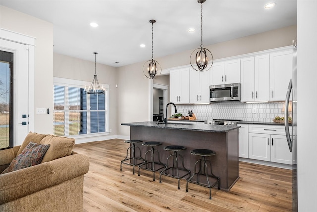 kitchen featuring sink, a center island with sink, white cabinetry, and pendant lighting