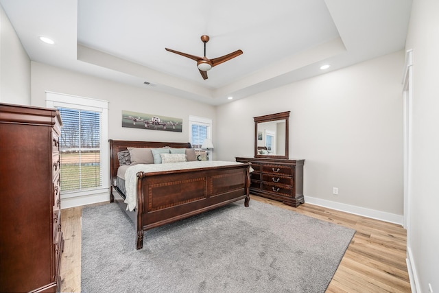 bedroom with ceiling fan, light hardwood / wood-style floors, and a raised ceiling