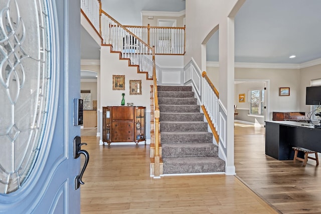 entrance foyer with ornamental molding, hardwood / wood-style floors, and a towering ceiling