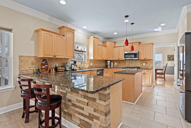 kitchen featuring stainless steel appliances, a kitchen island, dark stone countertops, light brown cabinets, and pendant lighting