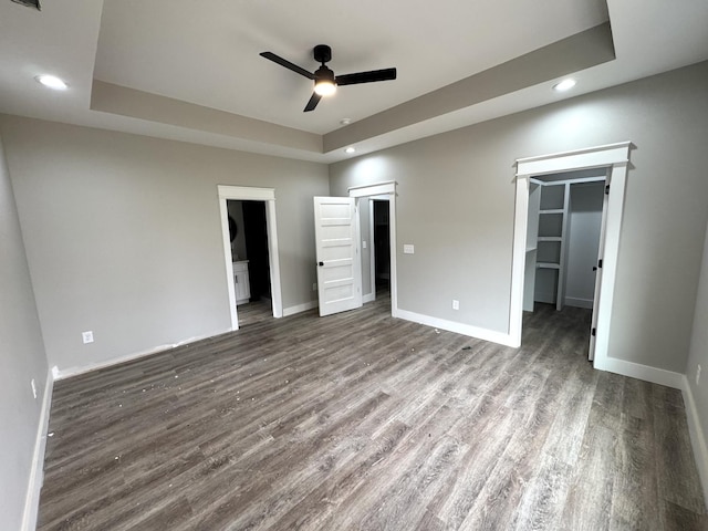 unfurnished bedroom featuring a walk in closet, a tray ceiling, a closet, and hardwood / wood-style flooring