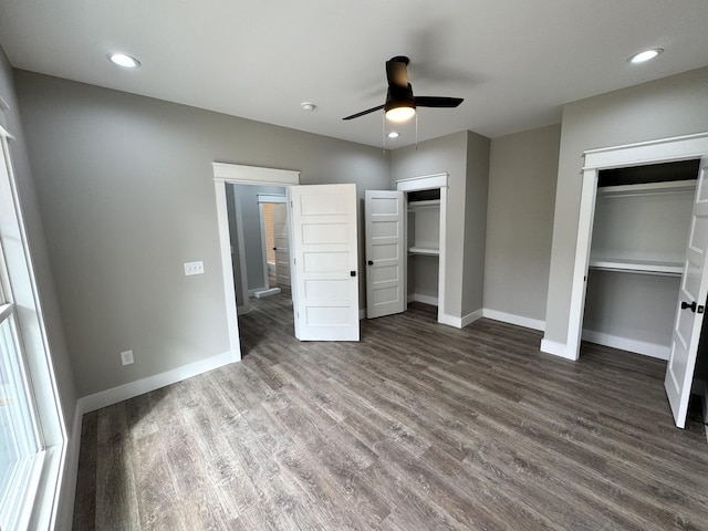 unfurnished bedroom featuring ceiling fan, multiple closets, and dark wood-type flooring