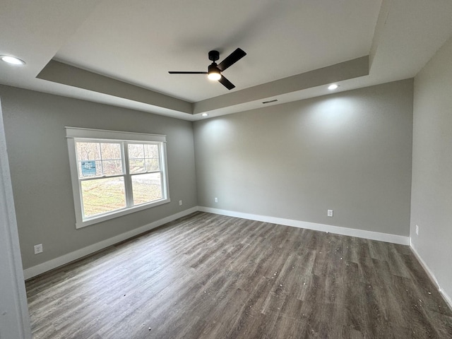 empty room with a raised ceiling, hardwood / wood-style flooring, and ceiling fan