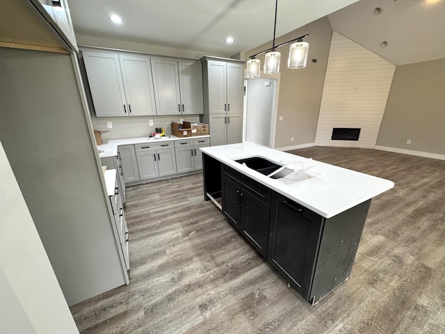 kitchen featuring a center island with sink, decorative light fixtures, sink, and dark hardwood / wood-style floors