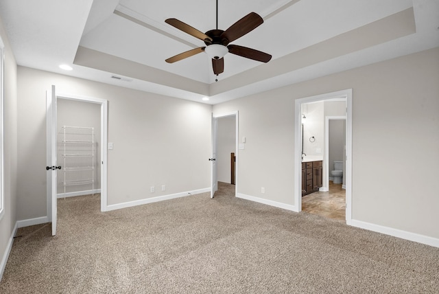 unfurnished bedroom featuring light carpet, ensuite bathroom, and a tray ceiling