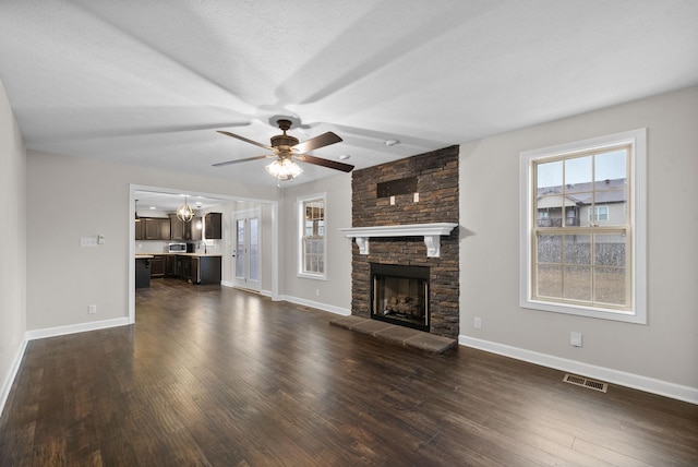 unfurnished living room featuring a wealth of natural light, dark wood-type flooring, a stone fireplace, and a textured ceiling