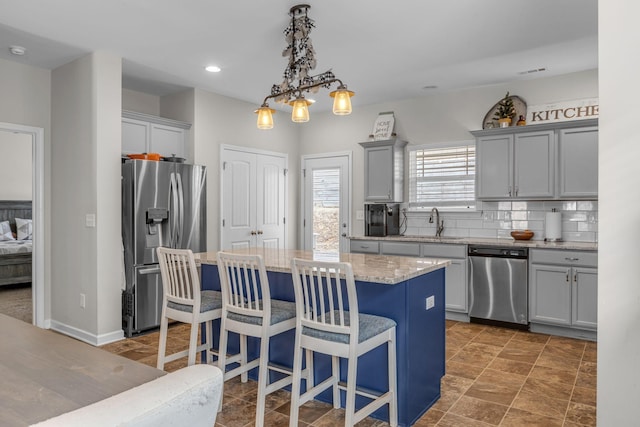 kitchen with appliances with stainless steel finishes, decorative light fixtures, a center island, backsplash, and a kitchen bar