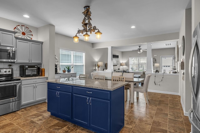 kitchen featuring appliances with stainless steel finishes, blue cabinetry, light stone counters, backsplash, and a kitchen island