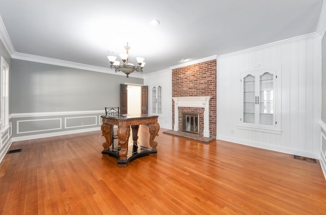 living room featuring built in shelves, a notable chandelier, a fireplace, hardwood / wood-style flooring, and ornamental molding