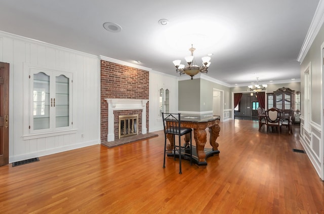 dining room with hardwood / wood-style flooring, crown molding, an inviting chandelier, and a brick fireplace