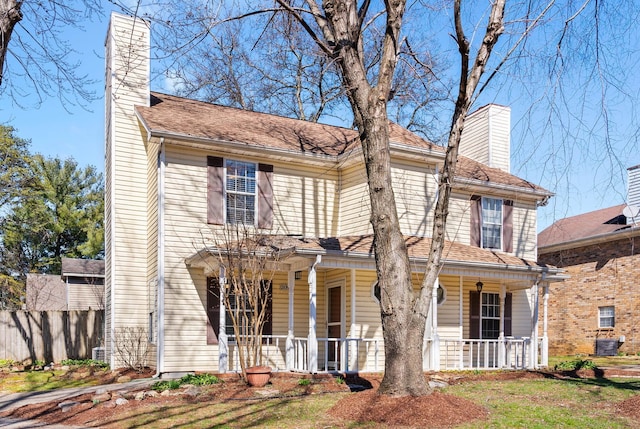 view of front facade featuring a porch, central AC, fence, roof with shingles, and a chimney