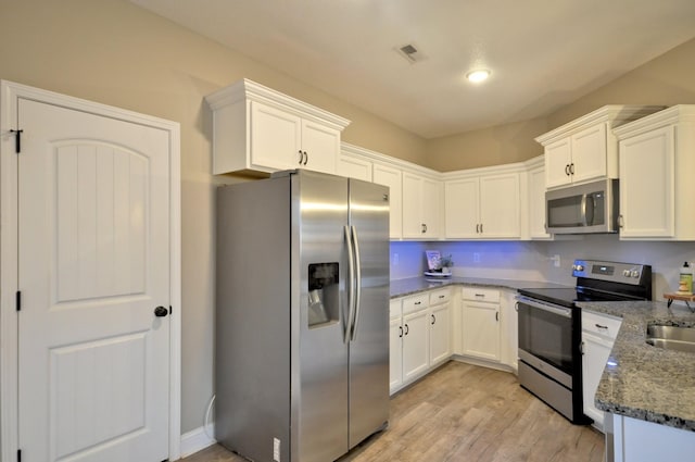 kitchen with dark stone countertops, stainless steel appliances, white cabinets, and light hardwood / wood-style flooring