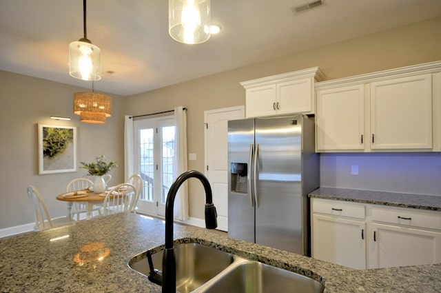 kitchen with sink, dark stone counters, stainless steel fridge, white cabinets, and hanging light fixtures