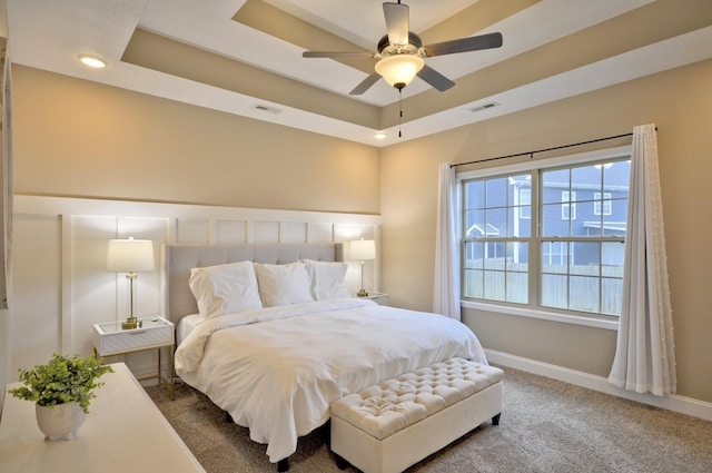 bedroom with a raised ceiling, carpet, and ceiling fan