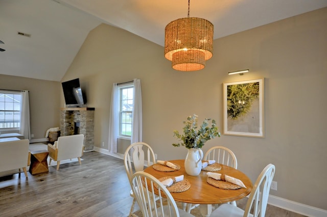 dining space featuring lofted ceiling, hardwood / wood-style floors, a chandelier, and a stone fireplace