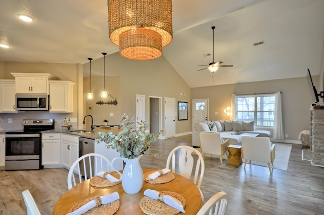 dining room with light wood-type flooring, high vaulted ceiling, sink, and ceiling fan with notable chandelier