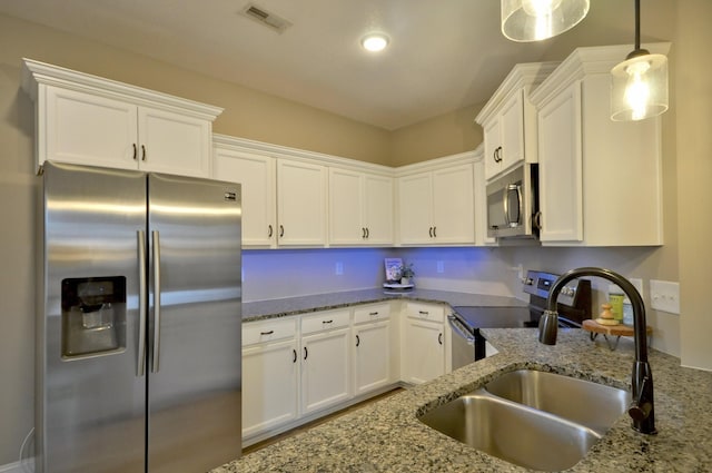 kitchen with hanging light fixtures, appliances with stainless steel finishes, white cabinetry, and light stone counters