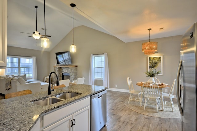 kitchen with appliances with stainless steel finishes, sink, light stone counters, a fireplace, and white cabinets