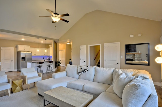 living room with ceiling fan, high vaulted ceiling, sink, and light hardwood / wood-style floors