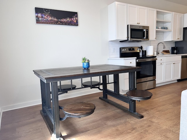 kitchen with white cabinets, light hardwood / wood-style floors, stainless steel appliances, and decorative backsplash