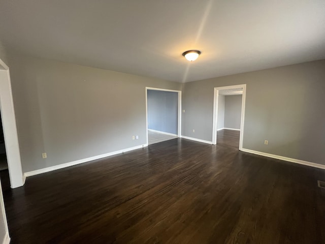 spare room with dark wood-type flooring, visible vents, and baseboards