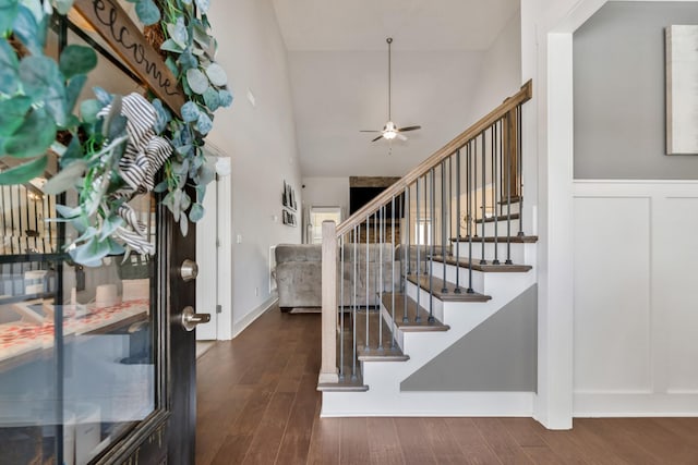 entrance foyer with a ceiling fan, a towering ceiling, dark wood-type flooring, stairs, and a decorative wall