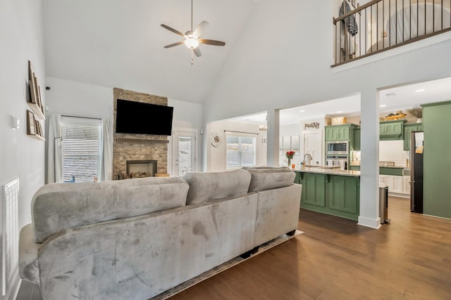 living area with high vaulted ceiling, dark wood-style flooring, ceiling fan, and a stone fireplace