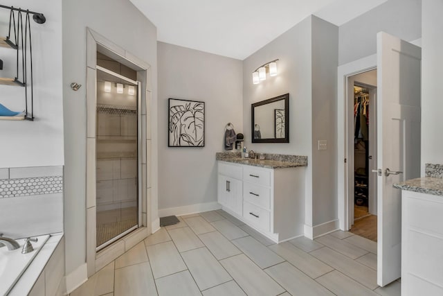 full bath featuring baseboards, a garden tub, a walk in closet, vanity, and a shower stall