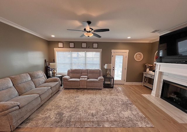 living area featuring light wood-style flooring, a premium fireplace, visible vents, a ceiling fan, and ornamental molding