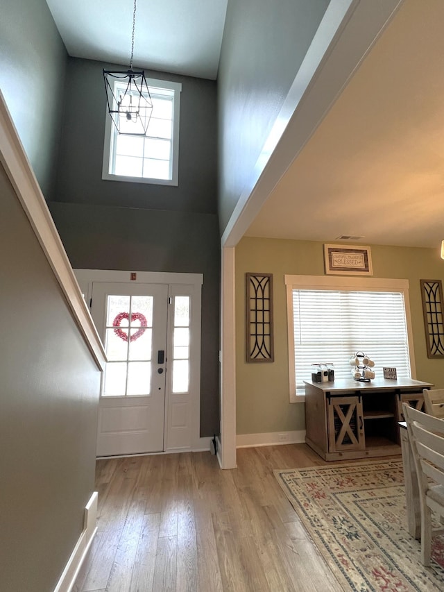 foyer with baseboards, light wood-style flooring, and a towering ceiling