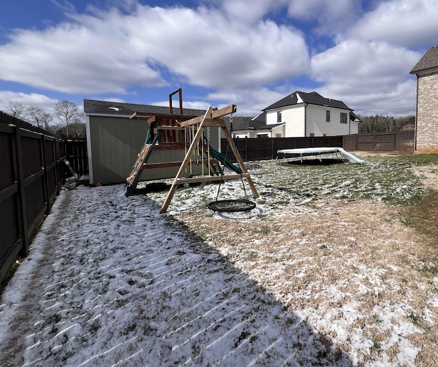 snow covered playground featuring a fenced backyard, a trampoline, and a playground