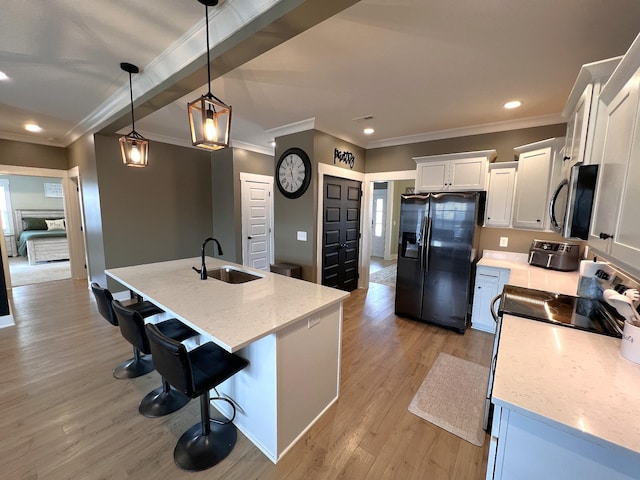 kitchen with decorative light fixtures, a center island with sink, stainless steel appliances, white cabinetry, and a sink