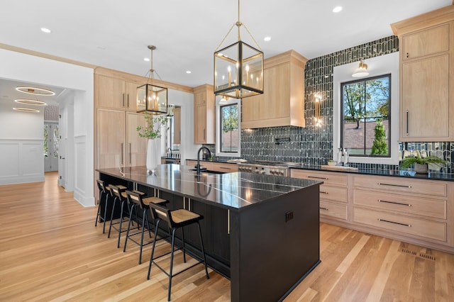 kitchen featuring a center island with sink, pendant lighting, a breakfast bar, and light brown cabinetry