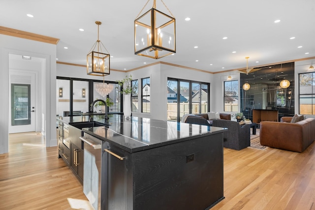 kitchen with sink, decorative light fixtures, light wood-type flooring, and a kitchen island with sink