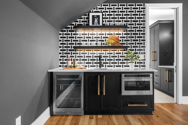 bar featuring light hardwood / wood-style flooring, sink, oven, and wine cooler