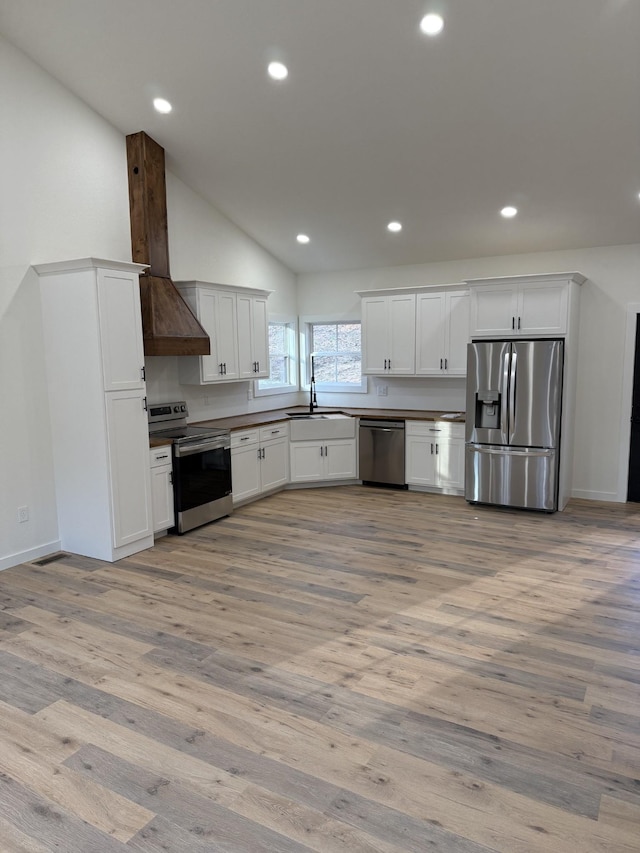 kitchen with sink, custom range hood, light hardwood / wood-style floors, stainless steel appliances, and white cabinets