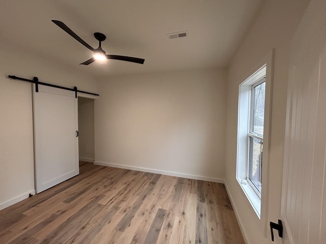 unfurnished bedroom featuring ceiling fan, a barn door, light wood-type flooring, and multiple windows