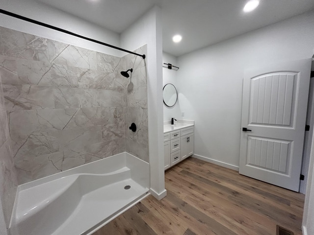 bathroom with hardwood / wood-style flooring, a tile shower, and vanity