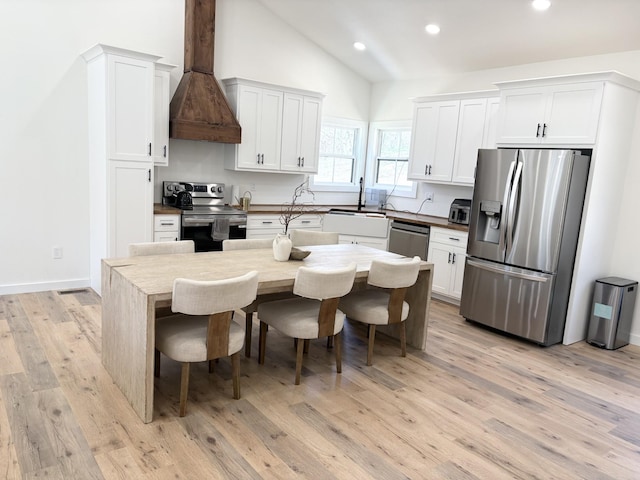 kitchen featuring custom exhaust hood, a sink, appliances with stainless steel finishes, light wood-style flooring, and lofted ceiling