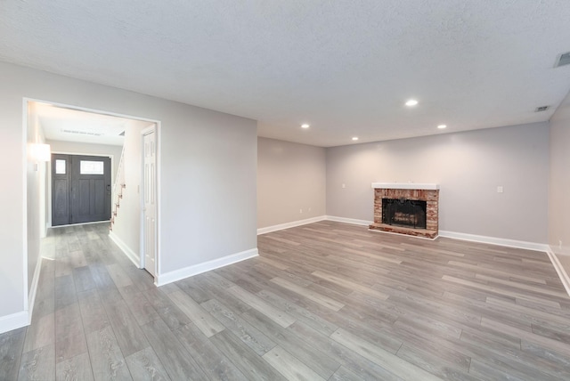 unfurnished living room featuring a fireplace, light wood-type flooring, and a textured ceiling