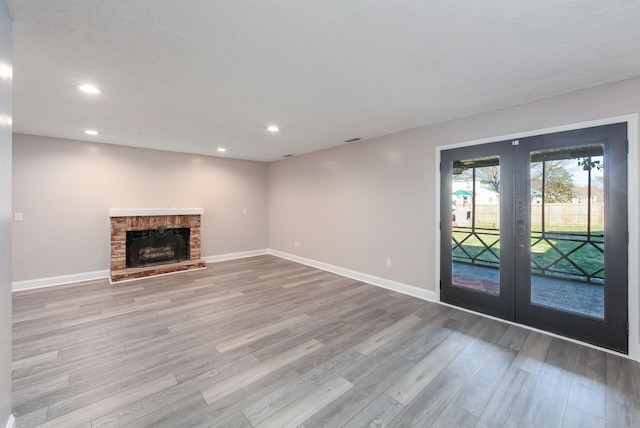 unfurnished living room featuring french doors, a brick fireplace, and light hardwood / wood-style flooring