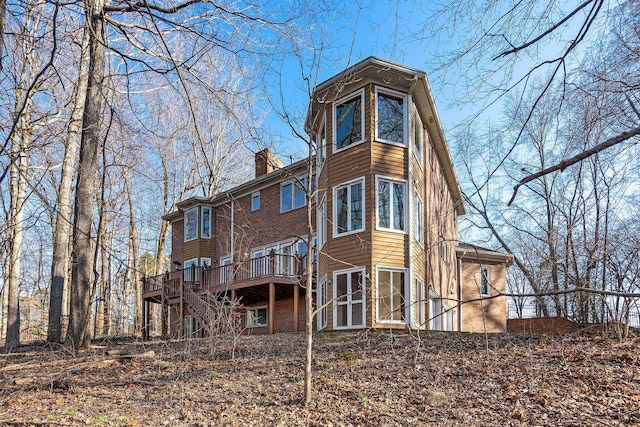 rear view of house featuring stairs, a chimney, a deck, and brick siding