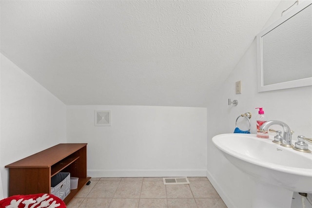 bathroom with vaulted ceiling, sink, tile patterned flooring, and a textured ceiling