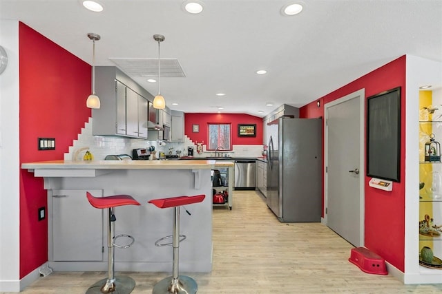 kitchen featuring light hardwood / wood-style floors, appliances with stainless steel finishes, a kitchen breakfast bar, and kitchen peninsula